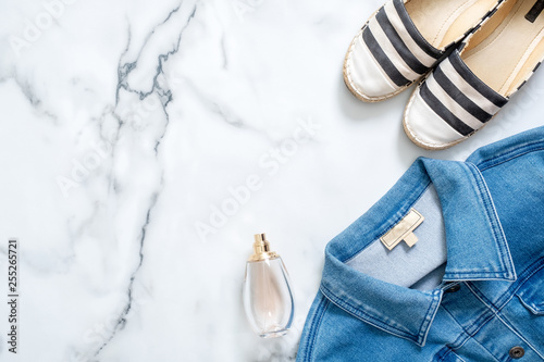 Denim jacket, bottle of perfume, striped summer sandals on marble background. Trendy flat lay composition, casual clothing of beauty fashion blogger, fashionable lady, tinder girl, hipster.