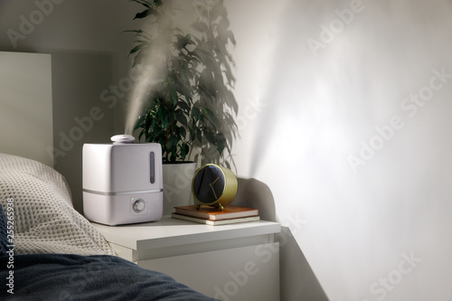 Aroma oil diffuser on the bedside table at night at home, steam from the air humidifier. Ultrasonic technology, increase in air humidity indoors.  photo