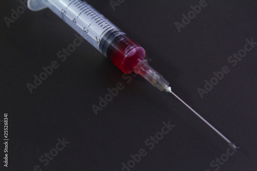 Medical syringe with needle and blood isolated on black and green background.