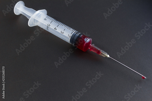 Medical syringe with needle and blood isolated on black and green background.