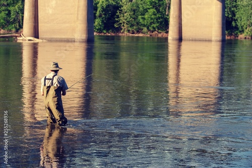Person  man  wading into river under a bridge to fly fish.  