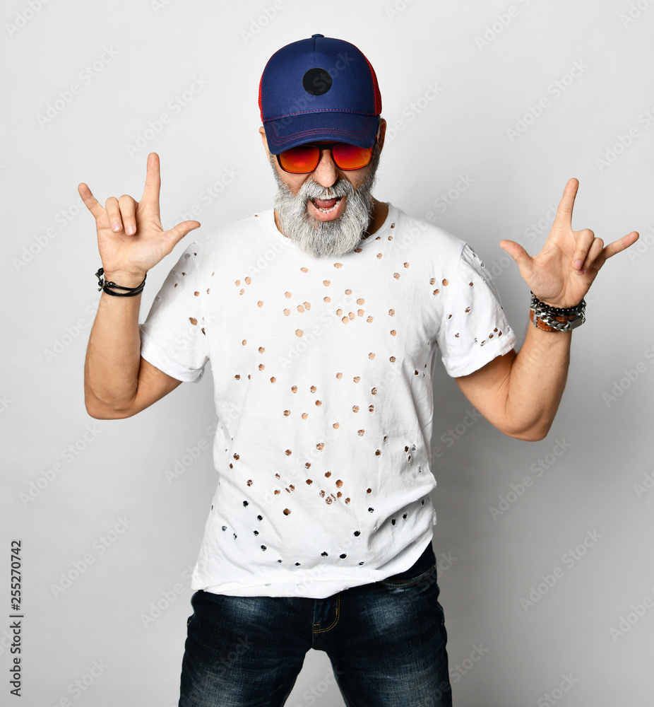 Old brutal man in designer t-shirt, blue jeans and baseball cap shows  rock'n'roll with both hands and shouts stylish fashionable men Stock Photo  | Adobe Stock