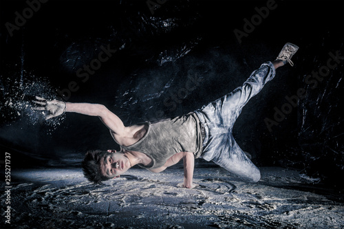 cool dirty сhinese  guy dancer in style of bboying doing complex tricks on floor in Studio filled with flour on black background. concept of space dance on surface of planet moon photo