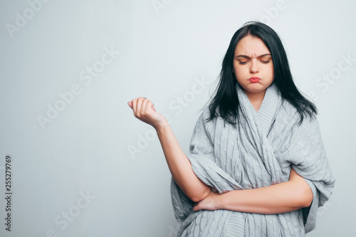 Upset brunette girl in a gray robe holding on to her stomach experiencing severe abdominal pain, diarrhea, menstruation. Woman suffers on gray studio background.