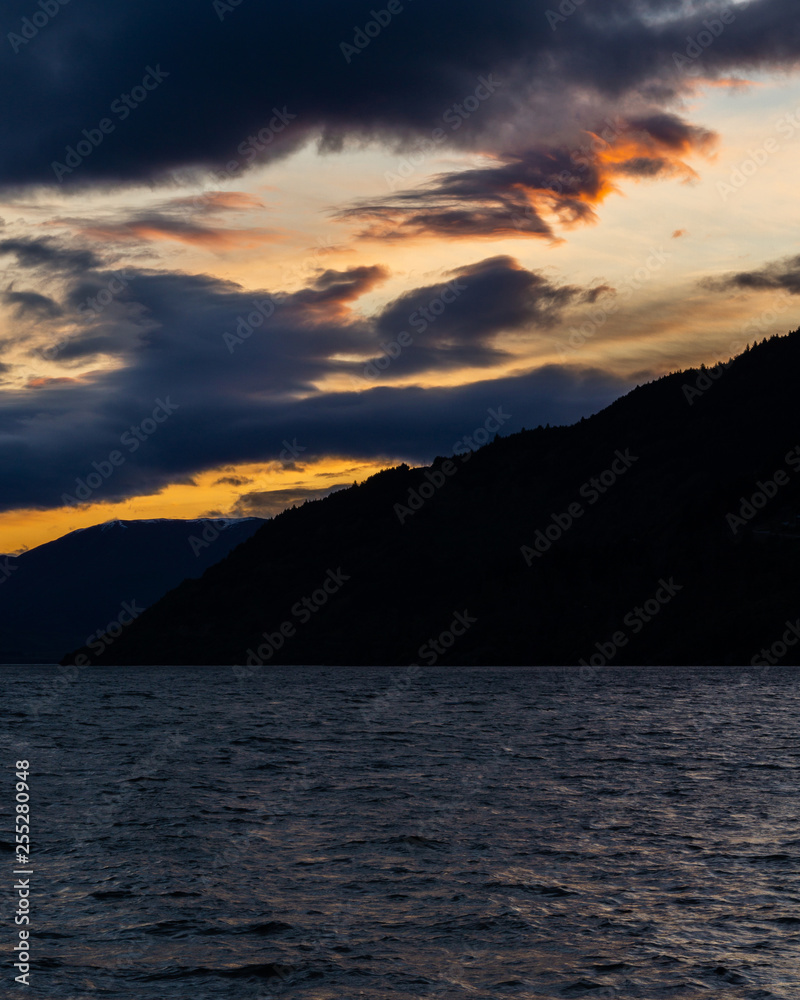 peaceful landscape during sunset with dramatic sky above the lake and mountain range, orange sky