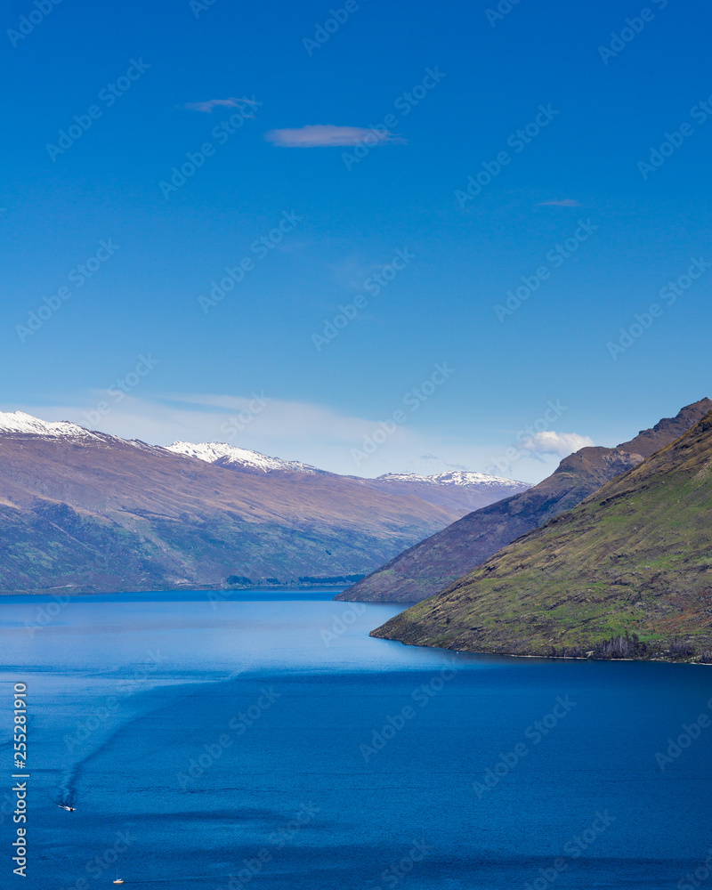 peaceful landscape during sunny day with calm sky above the lake and mountain range, small boat on a lake