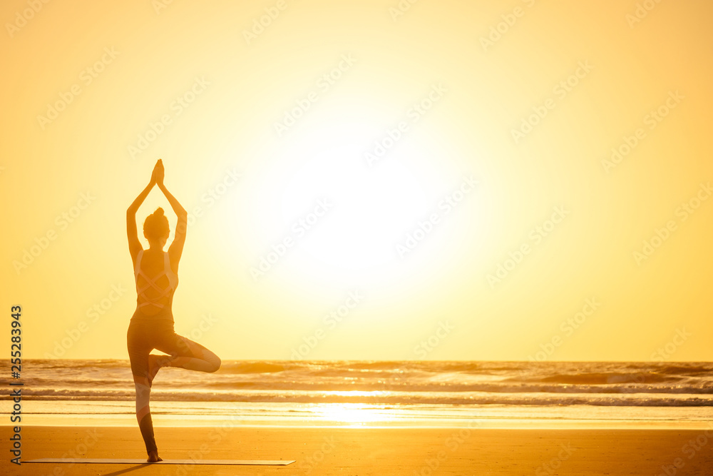 Silhouette of young woman in a stylish suit for yogi jumpsuit doing yoga on the beach in pose copy space