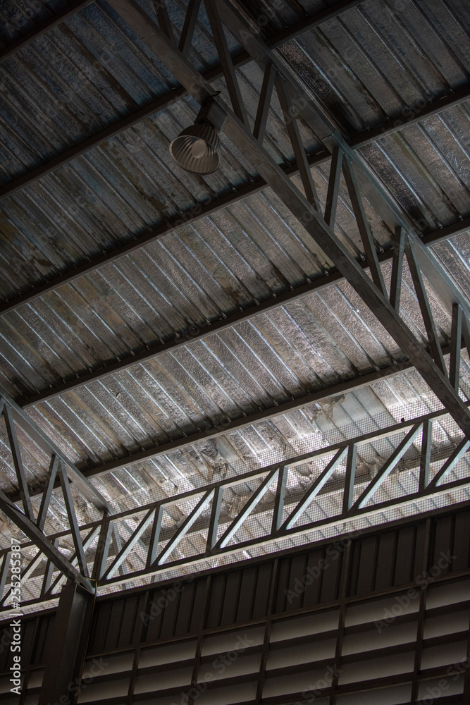 Obraz premium An interior space of a factory shop showing a scaffolding metal roof sheet with a framework of metal truss with sunlight goes through.