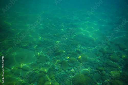 Gravel bottom in shallow green sea with areas of larger rocks and boulders and reflections from surface. © Daniel Poloha