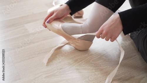Ballerina is tying ribbons on pointe shoes. Legs of a ballerina close-up., side view. 4k shooting.