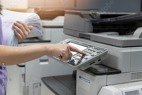 Fotografie Bussinesswoman using copier machine to copy heap of paperwork in office