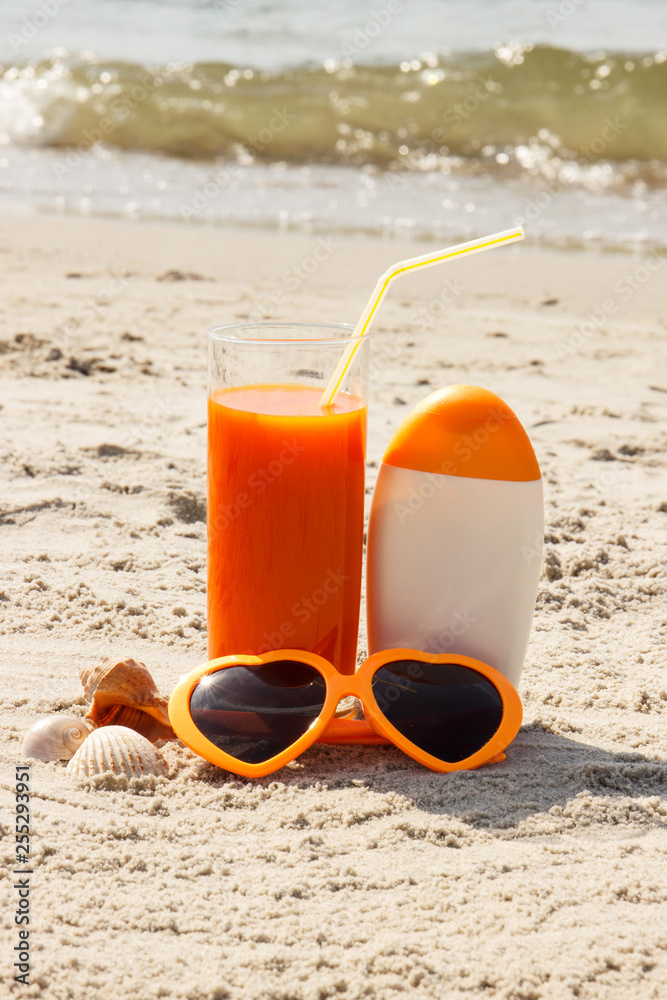 Carrot juice, sunglasses and sun lotion at beach, concept of vitamin A and beautiful, lasting tan Carrot juice, sunglasses and sun lotion at beach, concept of vitamin A and beautiful, lasting tan