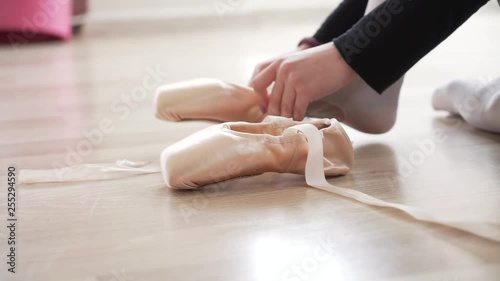 Ballerina is tying ribbons on pointe shoes. Legs of a ballerina close-up., side view. 