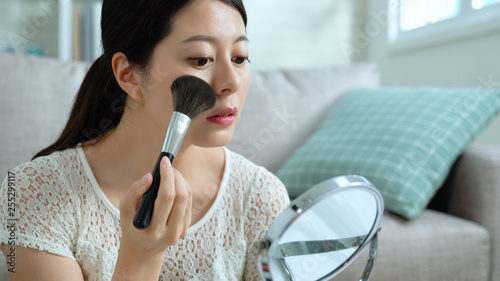 girl vlogger concentrated using brush and cosmetic on face looking at mirror in live streaming. young fashion blogger record makeup tutorial video for vlog. famous lady filming product advertisement