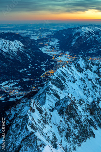 Tagesanbruch auf dem Gipfel der Zugspitze mit Blick auf das erleuchtete Garmisch Partenkirchen und ins Loisachtal
