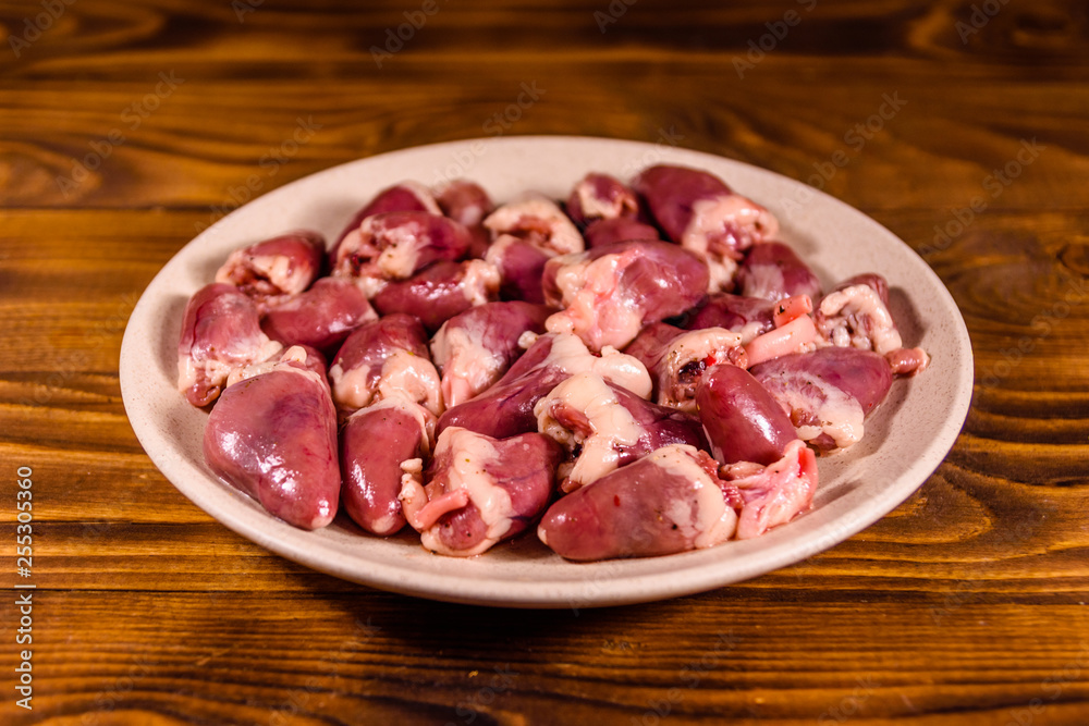 Ceramic plate with raw chicken hearts on wooden table Ceramic plate with raw chicken hearts on wooden table
