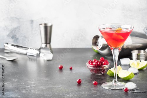 Classic alcoholic cocktail cosmopolitan with vodka, liqueur, cranberry juice, lime, ice and orange zest, gray bar counter background, bartender tols, space for text photo