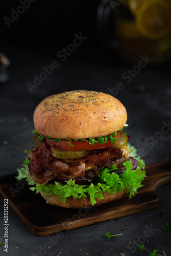 Homemade fresh beef burger on wooden board in dark mood photo style.