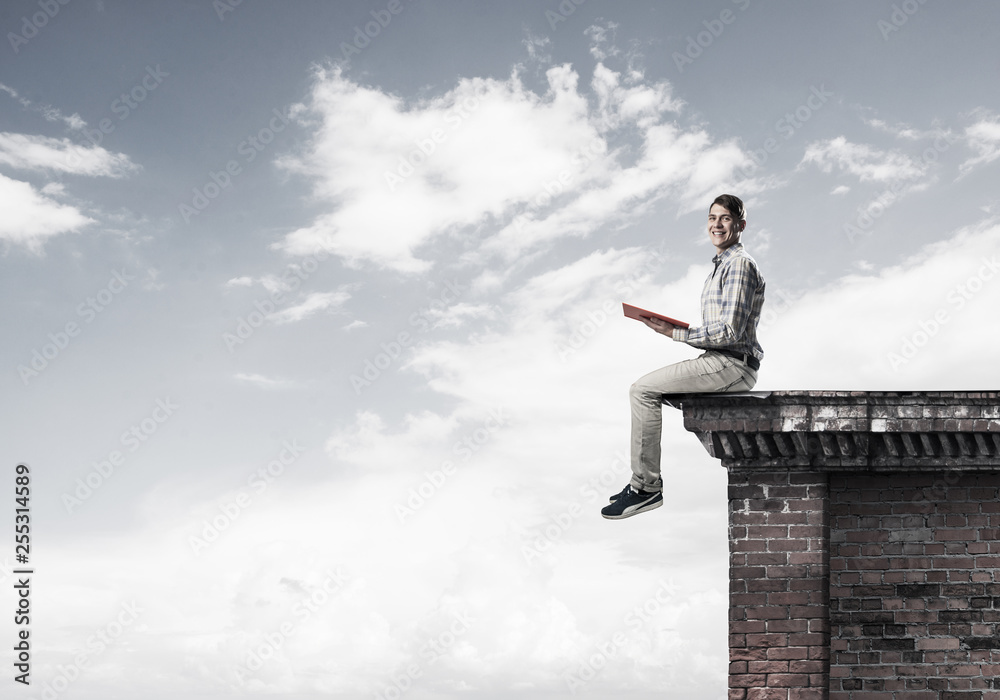 Man on roof edge reading book and cloudscape at background Man on roof edge reading book and cloudscape at background