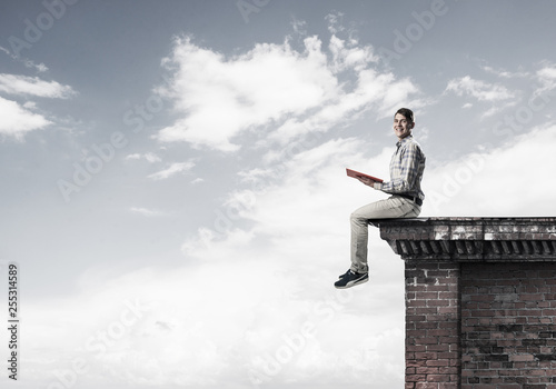 Man on roof edge reading book and cloudscape at background © adam121