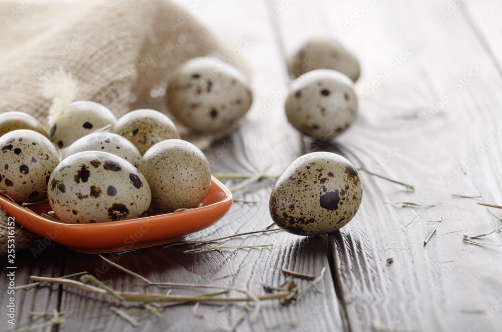 Obraz premium Fresh organic quail eggs in orange clay plate on wooden rustic kitchen table. Space for text
