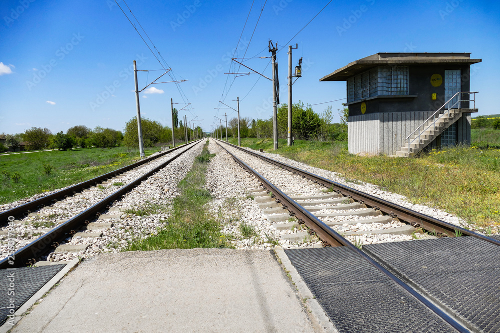 Obraz premium Railway electrified line in the plane. Two tracks are lost in the distance. Foreground - rail crossing. End of the rails - a small building.