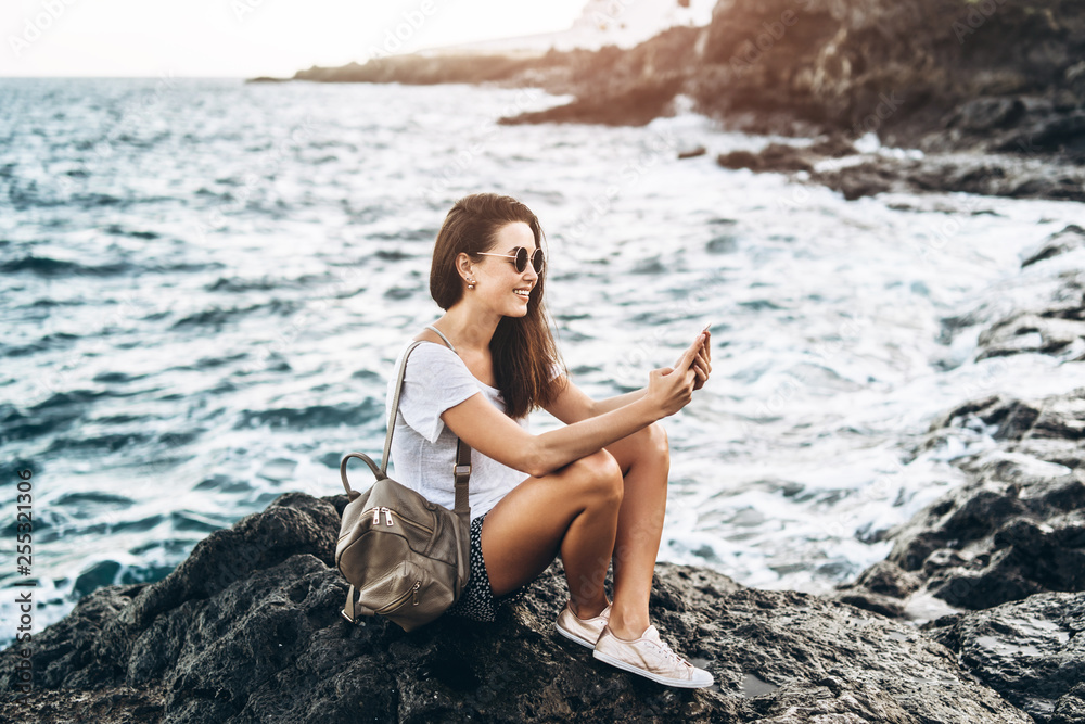 Pretty long hair tourist girl relaxing on the stones near sea.