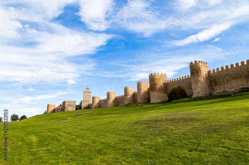 View of the medieval city walls surrounding the city of Avila, Spain, and the green lawn in front of Puerta del Carmen. Called the Town of Stones and Saints, Avila is a UNESCO World Heritage Site