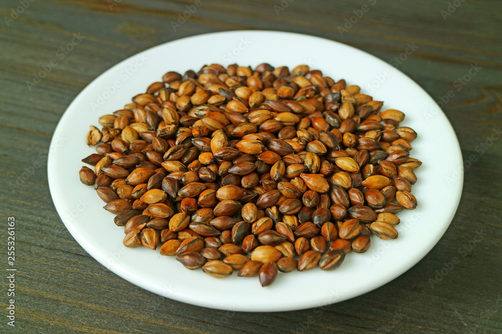 Plate of Roasted Barley for Japanese Barley Tea or Mugicha on Dark Brown Wooden Table Plate of Roasted Barley for Japanese Barley Tea or Mugicha on Dark Brown Wooden Table