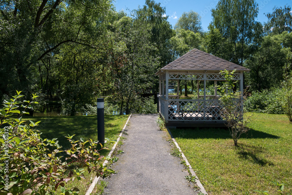 Path leading to wooden summerhouse standing among lush green trees and shrubs on bright sunny summer day Path leading to wooden summerhouse standing among lush green trees and shrubs on bright sunny summer day