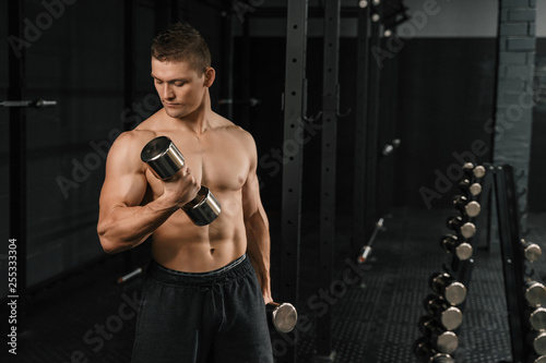 Handsome power athletic man bodybuilder doing exercises with dumbbell