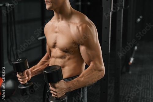 Close-up of a handsome young man lifting dumbbell.