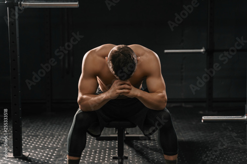 Strong sporty man sitting on gym bench suffering breakdown to overcome