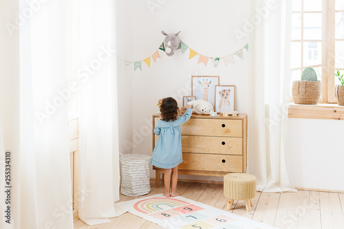 Little girl wearing light blue dress playing in children room scandinavian style.