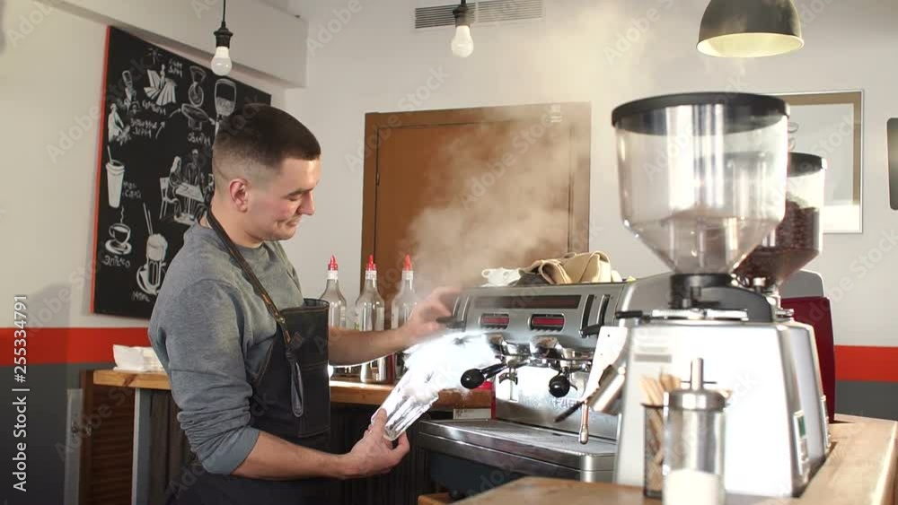 Portrait of a young man working in a coffee shop with modern equipment. Barista prepares hot fragrant cappuccino. Coffee machine in steam, barista preparing coffee at cafe. Portrait of a young man working in a coffee shop with modern equipment. Barista prepares hot fragrant cappuccino. Coffee machine in steam, barista preparing coffee at cafe.