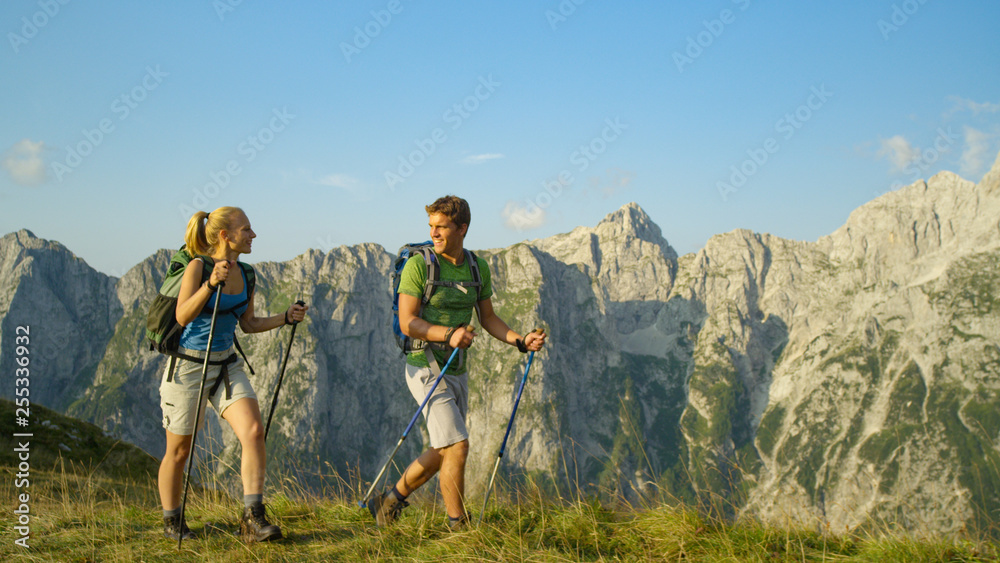 Smiling young Caucasian woman and man hiking in the breathtaking mountains.