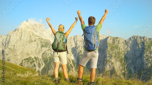 Unrecognizable young tourists celebrate hiking up the mountain in the Alps.