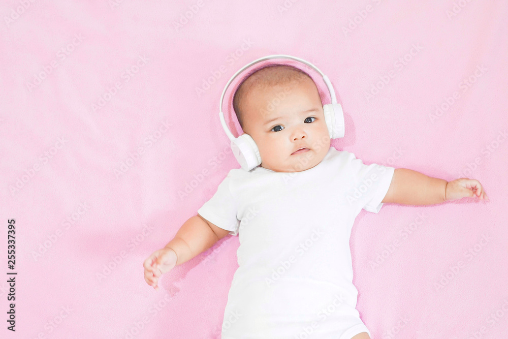 Asian baby girl wears white headphone and white shirt on pink background Asian baby girl wears white headphone and white shirt on pink background