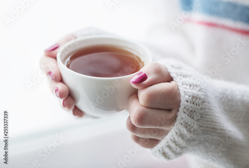 Tea drinking. The woman in a knitted, white pullover holds a cup of hot tea in her hands. Cozy weekends, winter drinks.