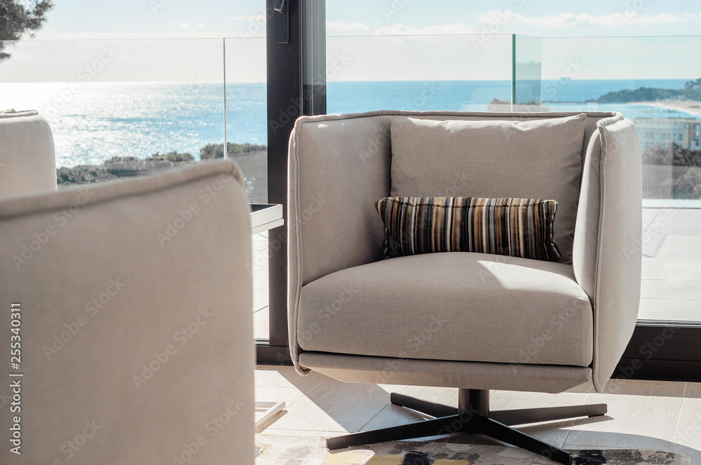 Fototapeta premium Modern living room interior with swivel chairs and coffee table, opposite window overlooking the sea. Details of the decor in a luxury home. Decor background.