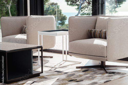Modern living room interior with swivel chairs and coffee table, opposite window overlooking the sea.  Details of the decor in a luxury home.  Decor background.
