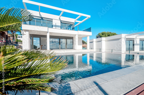 Luxury modern white house with large windows overlooking a Mediterian landscaped garden with palm trees and  blue swimming pool. High tech style villa. Vacation home or hotel. Modern loft design.ees a © steftach