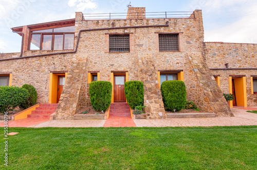 The facade of an old stone-built hotel house with a green lawn and separate entrances to the apartments.