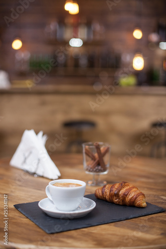 Hot coffee and croissant on coffee shop wooden table
