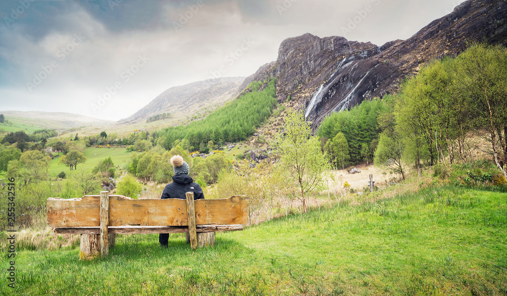 A girl sitting on the wooden bench and looking at the waterfall in Kenmare
