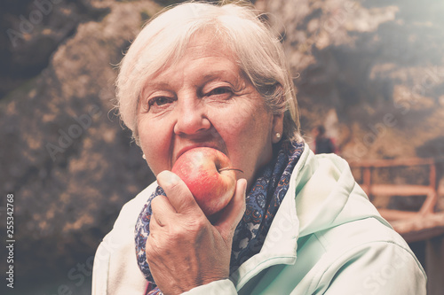 Healthy looking senior woman with grey hair eating apple outside in the park