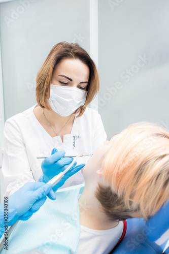 Young beautiful woman dentist treats teeth to woman patient
