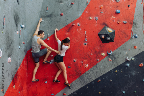 Beatiful woman in bouldering course. Her friend helping her to go through this complicated route.