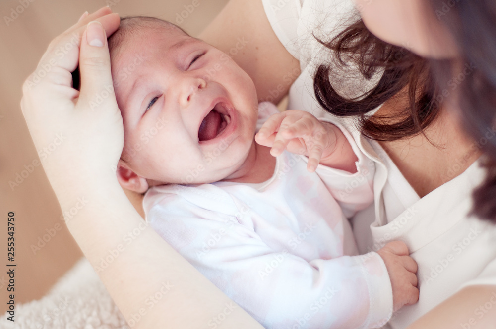 Mother holding her crying little baby. and checks forehead. Newborn baby is crying in mom's arms. Mother holding her crying little baby. and checks forehead. Newborn baby is crying in mom's arms.