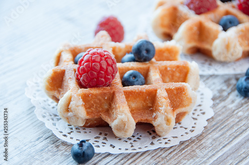 Traditional waffles with fresh raspberries and blueberries on lace doily on wooden background.
